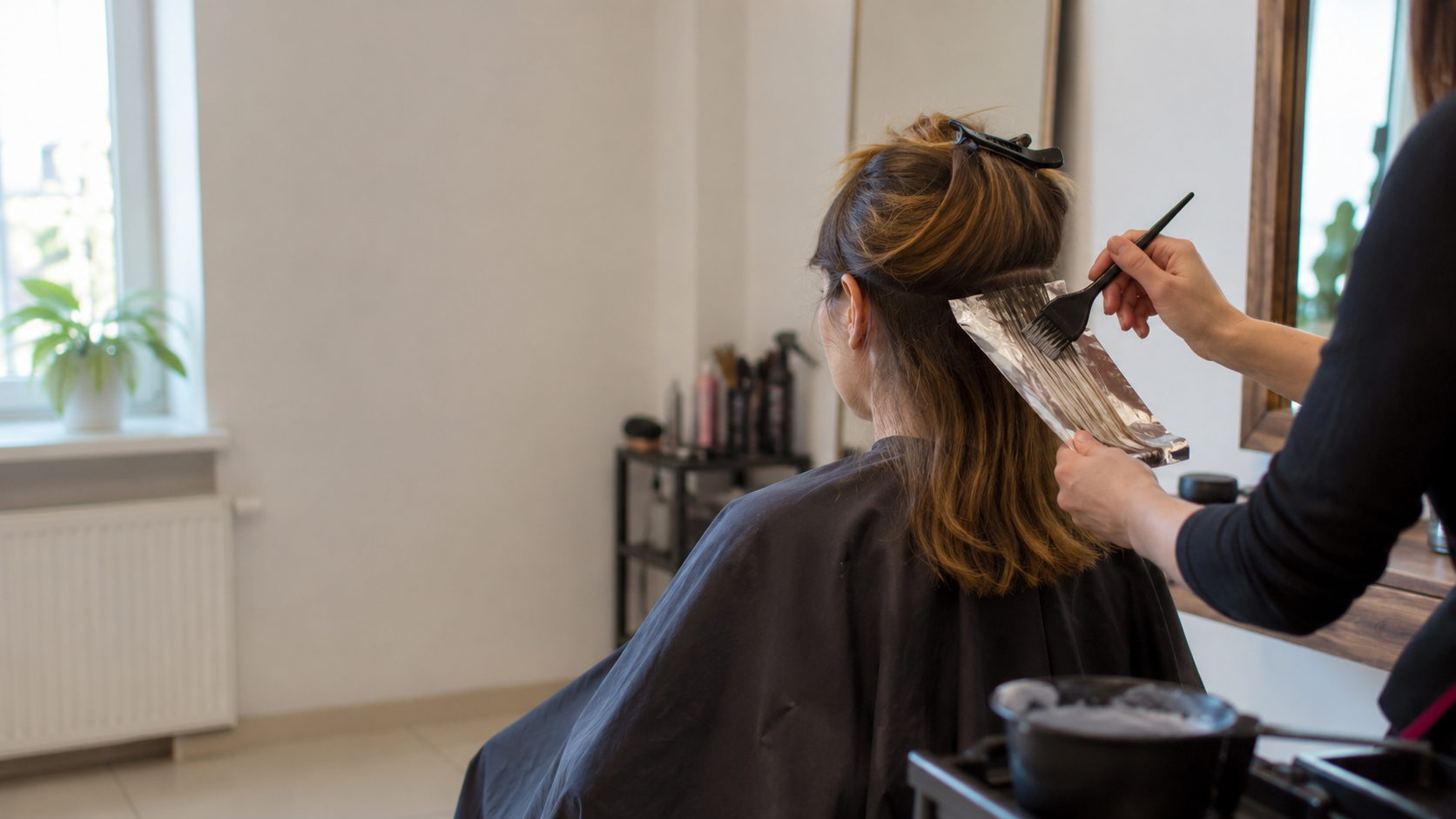 Stylistka nakłada preparat koloryzujący na wydzielone pasmo włosów klientki.